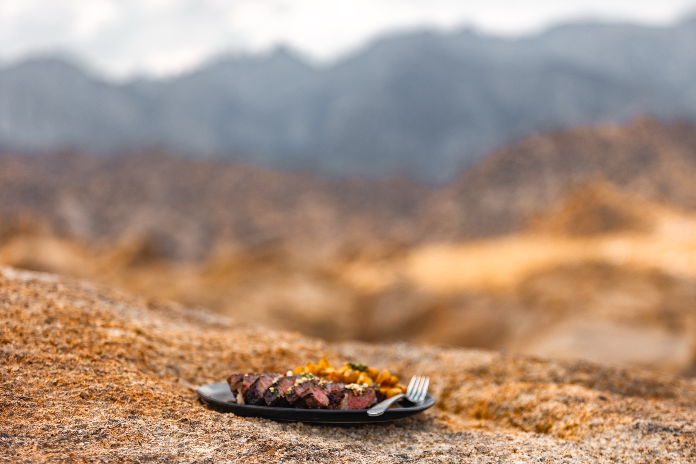 A plated steak resting on granite with mountains behind