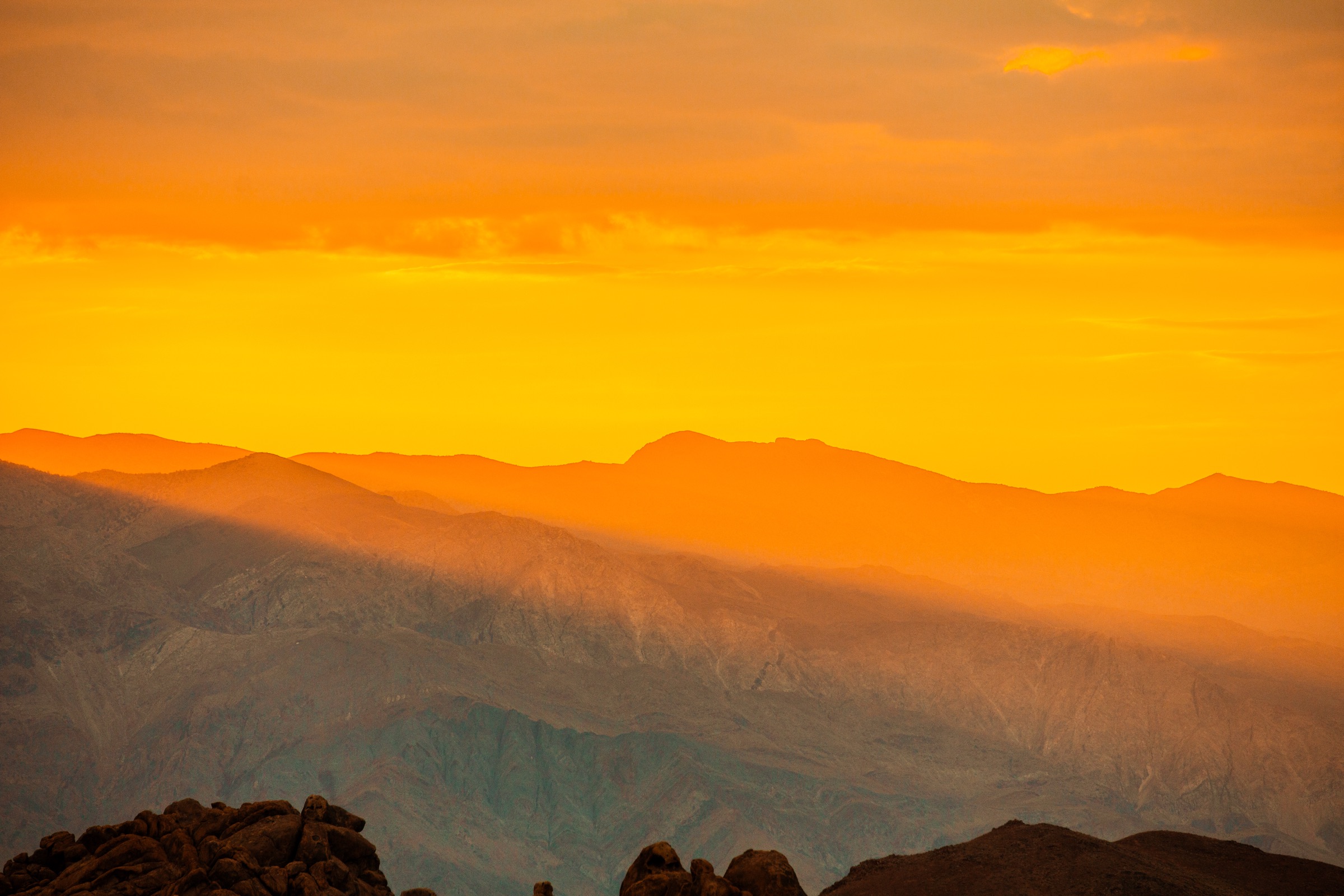 Layered mountain ridges under an orange sunset